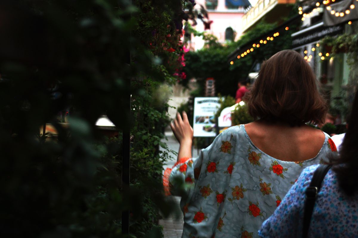 植物の並ぶ小道を歩く後ろ姿の女性